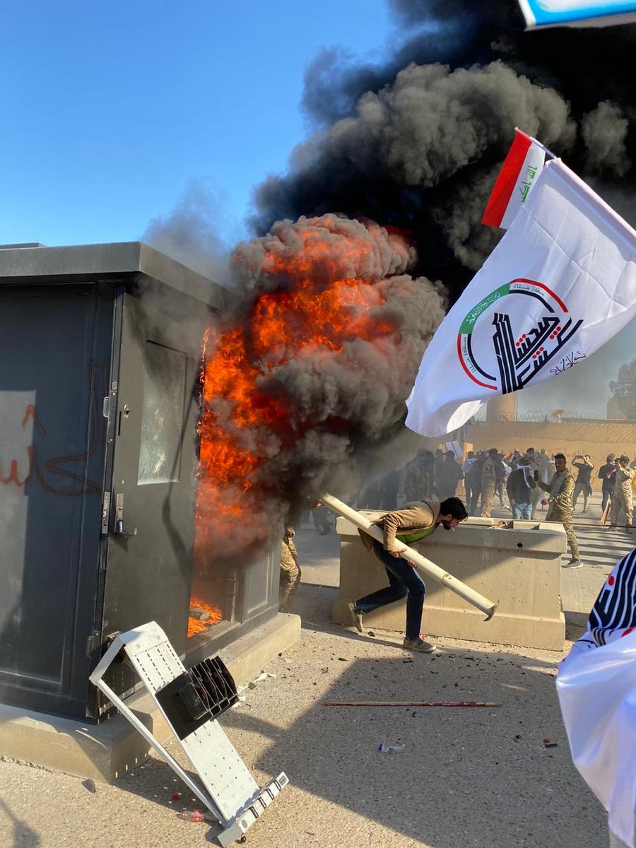 Security box near wall of U.S. Embassy complex in Baghdad set on fire by pro-Hezbollah protesters